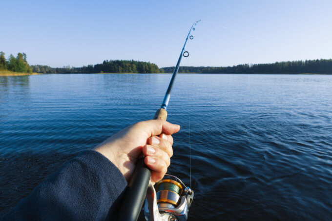 Fishing on a lake at sunset. Fishing rod with a reel in hand.