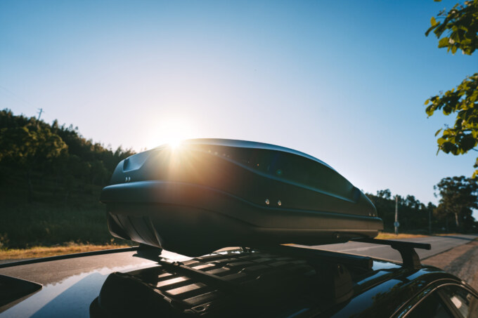 Car with black plastic rooftop cargo box or roof carrier for traveling. Removable storage container mounted on car roof rack