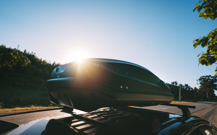 Car with black plastic rooftop cargo box or roof carrier for traveling. Removable storage container mounted on car roof rack