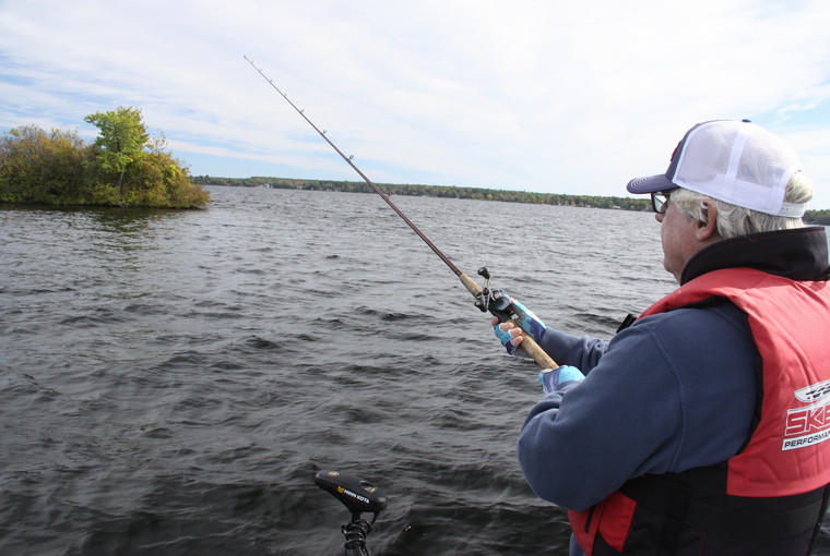 Angler casting a line off a boat into the lake on an overcast day.