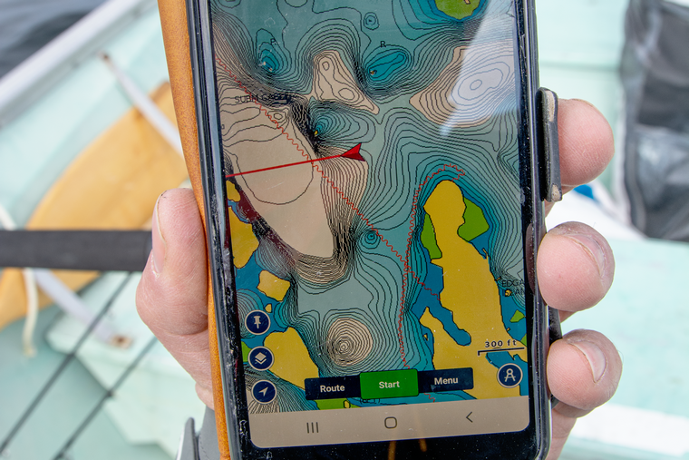 Angler in a boat using a fishing Navionics app to navigate a lake on a dreary day.