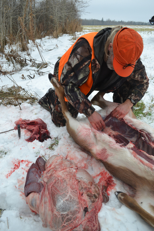 A hunter field-dressing a deer in a snowy winter landscape.