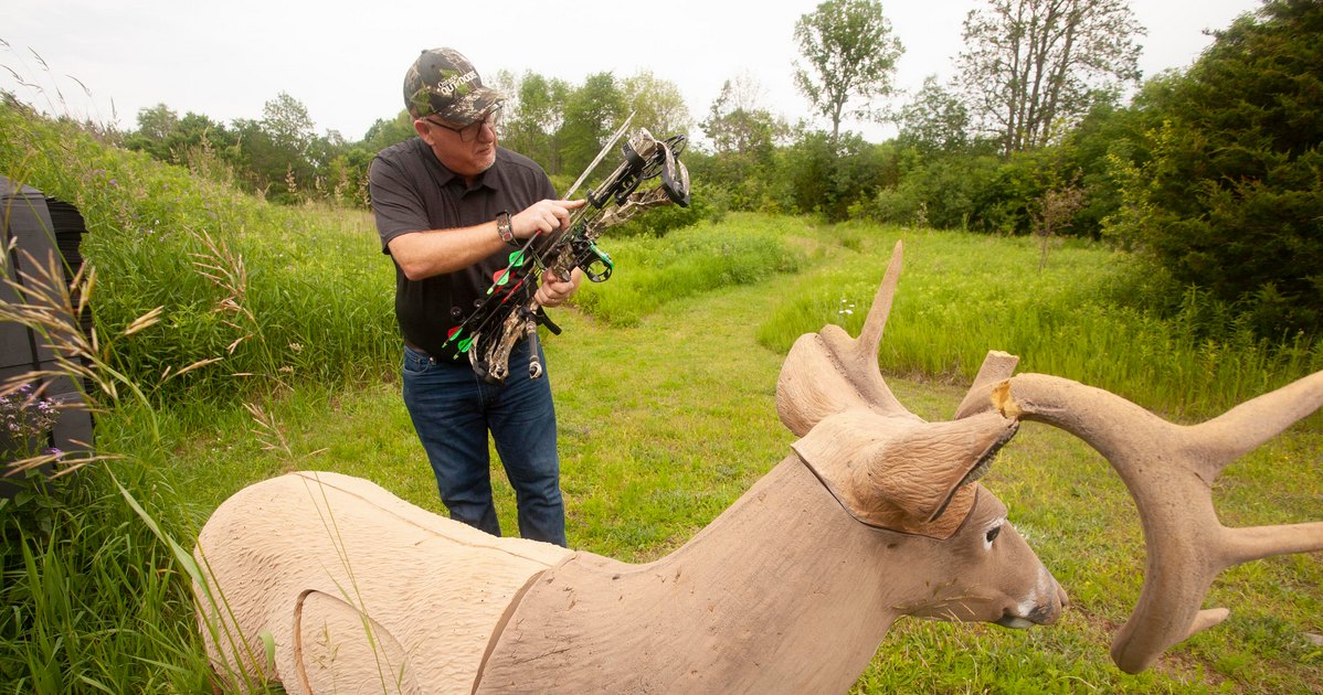 An archer removes an arrow from his quiver with a 3D archery deer target in view.
