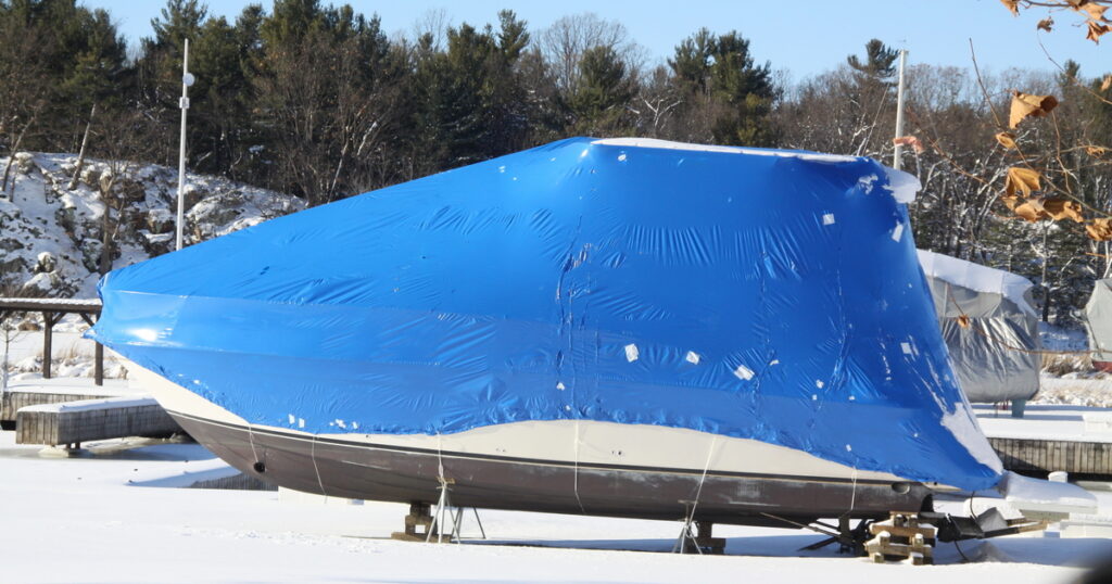 Winterized fishing boat wrapped in blue plastic, stored on land and out of the water for the off-season.