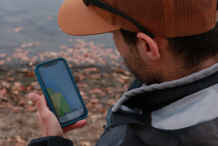 Shore angler holding a cell phone displaying a bathymetric map on the Garmin Navionics app.