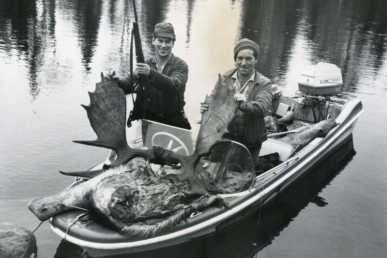 Two hunters in a boat with a moose rack and pelt. 