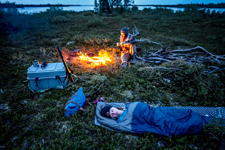 woman sleep beside a fire as the man looks off into the wild distance